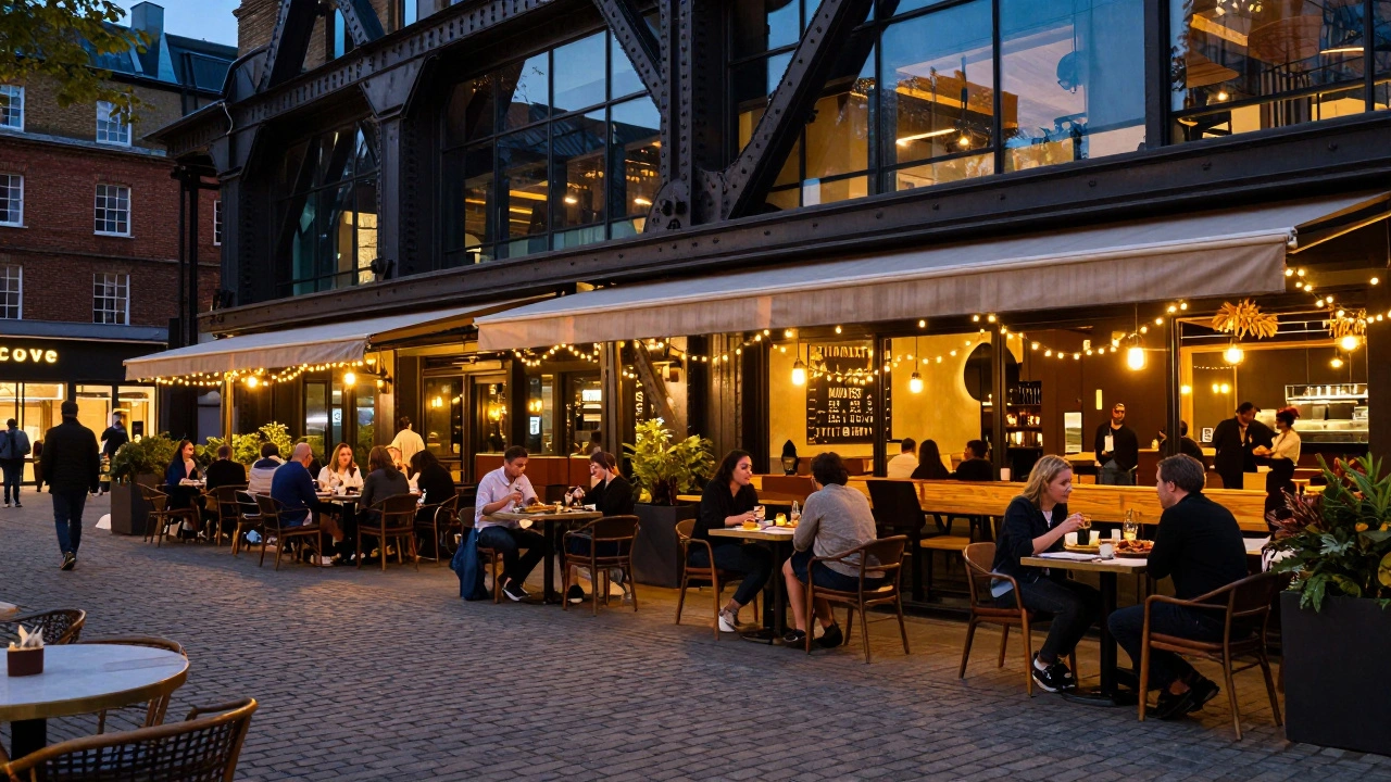 People dining at outdoor tables on a cobblestone plaza in King's Cross at dusk